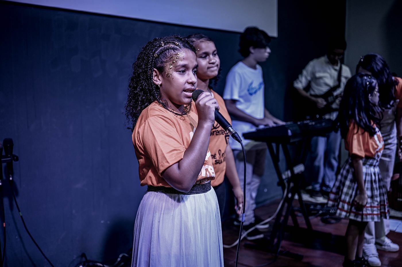 Criança cantando no palco com banda ao fundo
